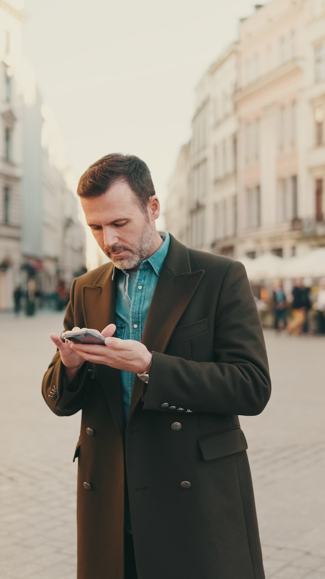 Middle aged man using map app on mobile phone on the old town background